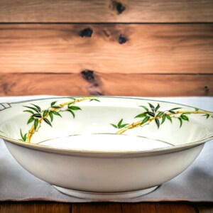 May include: A white ceramic serving bowl with a gold rim and a green and yellow bamboo design.
