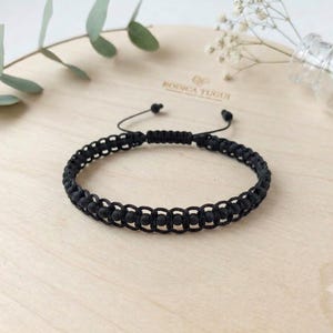 May include: A black macrame bracelet featuring a central row of small, round, matte black beads. The bracelet is constructed with a woven cord pattern and includes an adjustable sliding knot closure with two thin black cords extending from the back.