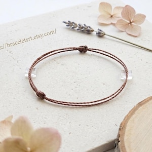 Può includere: Un braccialetto in cordino sottile di colore marrone con un design a doppio filo e due piccoli nodi scorrevoli per la regolazione. Il braccialetto è di forma circolare e include il testo https://braceletsrt.etsy.com/ stampato nell'angolo in alto a sinistra.