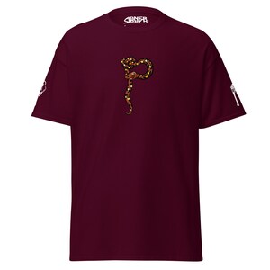 May include: Burgundy t-shirt with a detailed illustration of a snake in brown, gold, and black. The snake is in the centre of the shirt. The word "SIGNEЯ" is printed in white on the collar.