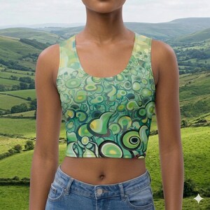 May include: A sleeveless crop top with a vibrant green and yellow abstract design. The pattern features swirling shapes and circular elements in various shades of green, with black outlines. The top is paired with blue jeans.