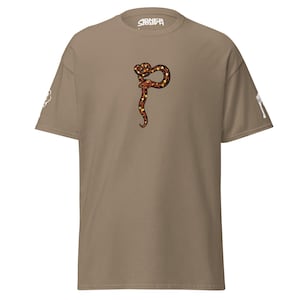 May include: A tan t-shirt featuring a colorful snake design in the center. The snake is depicted in shades of brown, orange, and yellow. The word "SIENER" is printed on the upper center of the shirt. Additional graphics are on the sleeves.