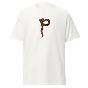 May include: White t-shirt with a brown, black, and yellow snake design. The snake is stylized and coiled. The t-shirt is made of a soft material, suitable for casual wear.