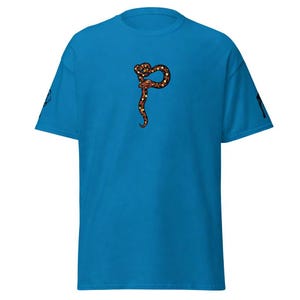 May include: A turquoise t-shirt with a snake design in brown, yellow, and black. The snake is coiled in a decorative pattern. The sleeves have a small graphic on each side.
