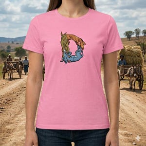 May include: Pink t-shirt featuring a colorful illustration of the letter "D" formed by cartoon donkeys. The donkeys are in shades of brown, blue, and green. The shirt is a solid pink color and is being worn by a person.
