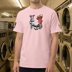 Op de afbeelding: Lichtroze t-shirt met een uniek grafisch ontwerp. Het ontwerp bevat abstracte vormen in blauw, rood en wit. Het shirt heeft korte mouwen en een ronde hals. Een kleine afbeelding staat op de linkermouw.