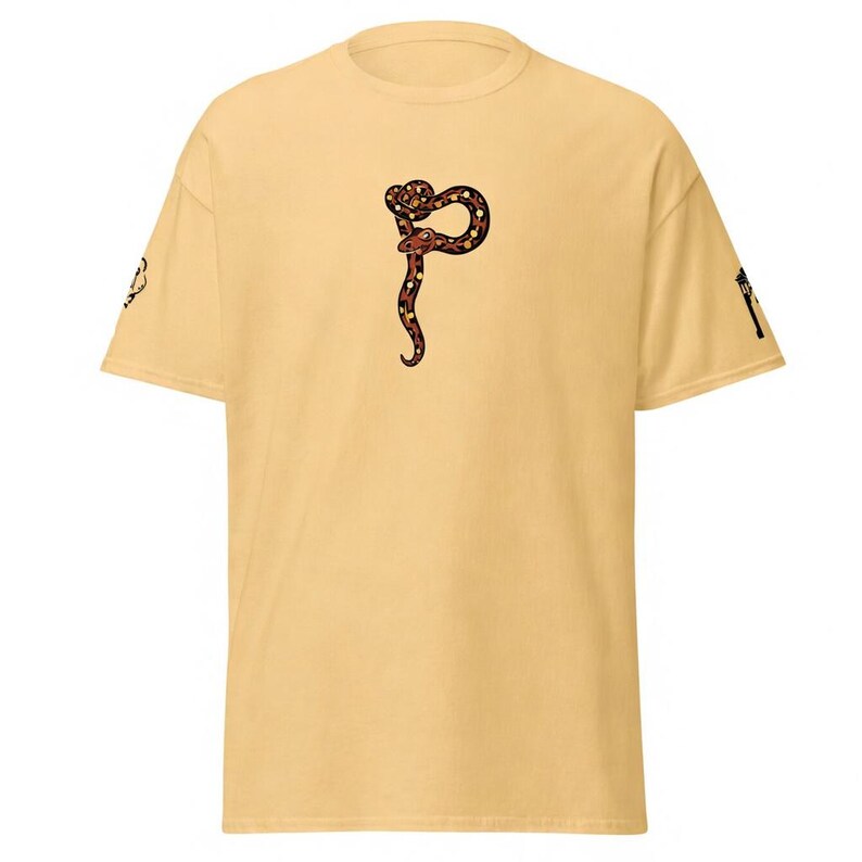 May include: Mustard-coloured t-shirt with a stylized snake design in brown, black, and red. The snake is in a curved, vertical position. The shirt has short sleeves and a crew neck.