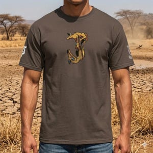 Può includere: T-shirt marrone con un'illustrazione stilizzata di uno sciacallo nei toni del marrone e dell'oro. La maglietta ha un girocollo e maniche corte. C'è una grafica bianca sulla manica sinistra.
