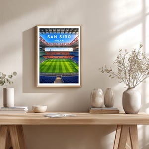 May include: A framed wall art print featuring a vibrant, high-angle view of the San Siro stadium in Milan. The image displays a bright green soccer pitch, blue and orange seating sections, and a structural roof, with the text SAN SIRO MILAN.