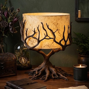 May include: A table lamp featuring a base shaped like dark brown tree roots and a trunk that branches upwards to support a cylindrical, textured, off-white lampshade. The shade is encircled by dark brown, branch-like decorative elements.