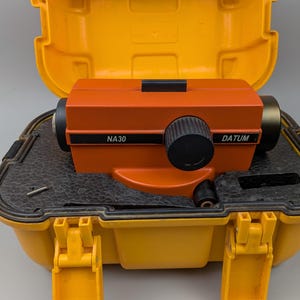 Peut inclure: Un niveau automatique de chantier orange NA30 DATUM avec un bouton de réglage noir, logé dans une mallette de transport rigide en plastique jaune vif avec un rembourrage intérieur en mousse noire et deux loquets de verrouillage.