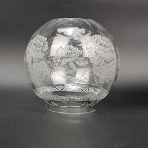 May include: A clear glass globe lamp shade featuring an etched floral pattern of blooming flowers and foliage. The spherical shade has a circular opening at the top and a smaller, fluted base designed for attachment to a light fixture.