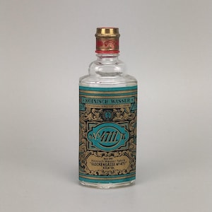 May include: A clear glass bottle of 4711 Echt Kölnisch Wasser with a gold and teal label featuring ornate scrollwork. The label displays the text 4711, Original Eau de Cologne, and Kölnisch Wasser Fabrik Glockengasse No 4711. It has a gold cap.