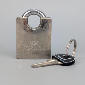 以下が含まれることがあります： 丸みを帯びたシャックルと前面にSTERLINGの刻印がある銀色の金属製南京錠。白いスマイリーフェイスのグラフィックが描かれた黒いプラスチック製のヘッドを持つ金属製の鍵と、小さな金属製のキーリングが付属しています。