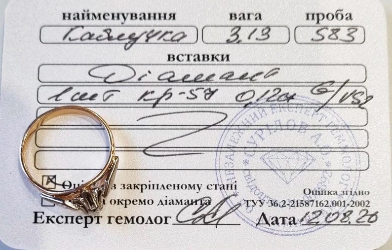 May include: A gold ring with a single diamond setting placed on a white certification document. The document features handwritten text including 3.13 weight, 583 purity, and diamond specifications, along with a circular blue ink stamp and a date.