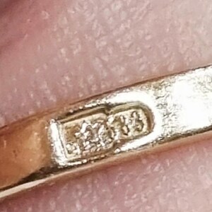May include: A gold ring band featuring a rectangular hallmark stamp on the interior surface. The stamp displays a five-pointed star symbol positioned to the left of the number 585, indicating the gold purity of the metal band.