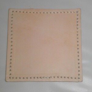 May include: A square piece of light brown leather with a decorative stitched border.