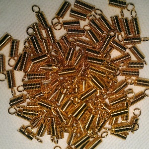 May include: A large pile of gold-colored metal spring cord ends. The cord ends have a small loop at one end.