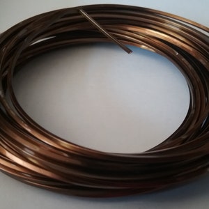 May include: Coiled roll of thin, flat, copper-colored metal strips. The strips are tightly wound, creating a circular shape. The metal has a reflective surface, and the color is a warm, dark brown. The material appears to be flexible and suitable for crafting or decorative purposes.