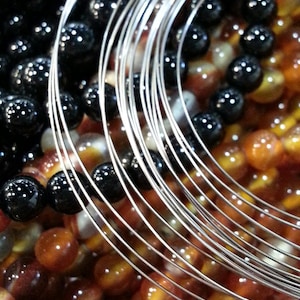 May include: A close-up of a silver wire wrapped around black and brown beads. The wire is arranged in a circular pattern, creating a layered effect. The beads are arranged in a random pattern, creating a visually appealing contrast.
