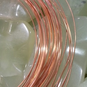 May include: A close-up of a coil of copper wire, with a shiny, metallic finish. The wire is wound tightly together, creating a circular shape. The wire is resting on a white, textured surface.