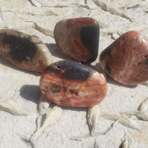 May include: Four smooth, polished stones with a mix of red, black, and white swirling patterns. The stones are on a light gray background.