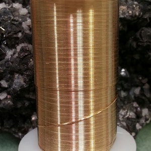 May include: A spool of gold-colored wire wrapped around a white plastic base. The wire is shiny and has a smooth texture.