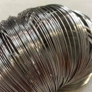 May include: A close-up of a silver metal coil of wire. The wire is tightly wound and forms a spiral shape.