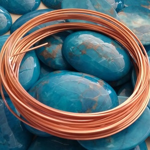 May include: A coil of copper wire, approximately 20 gauge, is shown on a bed of turquoise cabochons. The wire is shiny and has a reddish-brown color.