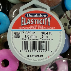 May include: A spool of Beadalon Elasticity elastic cord. The label is white with a red and blue stripe and text that reads "Elastic Cord". The cord is .039 inches, 1.0 mm, and 5 m. The background is a collection of colorful beads.