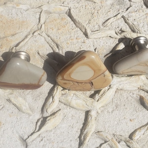 May include: Three stone cabinet knobs with a silver finish. The knobs are shaped like irregular triangles and have a light brown, beige, and white marbled pattern.