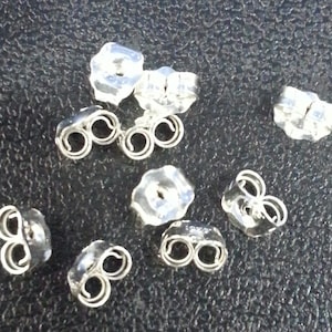 May include: A close-up of a group of silver earring backs. The backs are made of metal and have a small loop on the top. They are designed to be used with stud earrings.