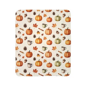 Puede incluir: Una manta rectangular con fondo color crema que presenta un patrón repetitivo de calabazas naranjas, calabazas verdes, bellotas marrones, piñas, hojas de arce, ramas de canela y tazas humeantes de café o té.