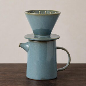 Peut inclure: Un ensemble de cafetière à verser en céramique avec un émail bleu-vert sourd. L'ensemble se compose d'un égouttoir conique avec des crêtes internes reposant sur une carafe cylindrique dotée d'un petit bec verseur et d'une anse incurvée.