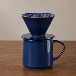 May include: A deep blue ceramic coffee dripper sits securely atop a matching blue ceramic mug. The dripper features internal vertical ridges and a wide rim, while the mug has a sturdy handle and a smooth, glossy finish throughout the set.