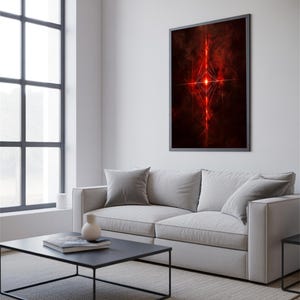 May include: A framed abstract art print with a dark background and a central, glowing red design. The artwork is displayed above a light gray sofa in a modern living room setting. The room also features a black coffee table and a large window.