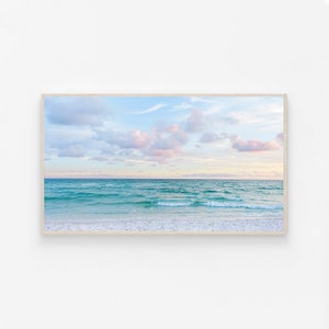 May include: A photograph of a beach scene with turquoise water and white sand. The sky is a light blue with fluffy white clouds and a hint of pink.