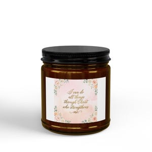 Könnte beinhalten: Ein braunes Glas mit schwarzem Deckel. Das Glas hat ein weißes Etikett mit dem Text "I can do all things through Christ who strengthens me" in goldener Schrift. Das Etikett ist von einem Aquarell-Blumenmuster in Rosa und Pfirsich umgeben.