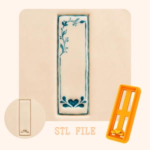 Può includere: Un tagliabiscotti rettangolare con un motivo floreale blu e un cuore in basso. Il disegno è su sfondo bianco. Sono mostrati anche una cornice di plastica arancione e un piccolo tagliabiscotti rotondo con un cuore. Il testo "STL FILE" è visibile.