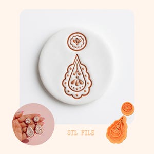 Op de afbeelding: Een witte oorbelvorm met een gedetailleerde druppelvorm en een kleinere cirkelvormige bovenkant. De vorm staat op een wit oppervlak, met een kleine afbeelding van de oorbellen en de tekst "STL FILE".