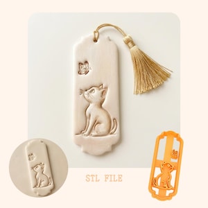 May include: A beige bookmark with a cat and butterfly design, featuring a gold tassel. The cat is looking up at a butterfly. The text "STL FILE" is printed below the bookmark. An orange plastic mold of the bookmark is also shown.