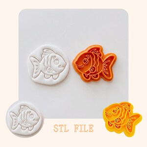 May include: An orange plastic fish-shaped cookie cutter and a white imprint of the same design. The cutter has detailed fins and a smiling face. The text "STL FILE" is printed in the bottom centre.