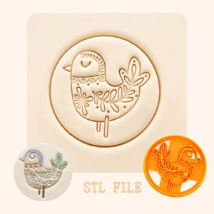 May include: A beige bird-shaped cookie stamp with a detailed floral design. The stamp is in a circular shape, with the text "STL FILE" below. A finished cookie and an orange plastic cutter are also shown.