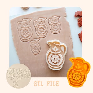 Puede incluir: Un cortador de galletas de plástico naranja brillante con forma de jarra junto a una masa extendida con cuatro diseños de jarra impresos. La masa muestra patrones florales y motivos de hojas detallados. El texto STL FILE aparece en naranja.