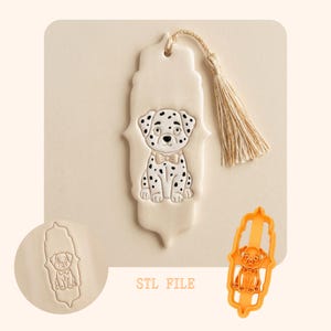 Op de afbeelding: Crèmekleurige boekenlegger met een Dalmatische puppy-ontwerp met zwarte vlekken en een vlinderdas. De boekenlegger heeft een kwast en wordt vergezeld door een bijpassende koekjesvorm. De tekst "STL FILE" is op het oppervlak gedrukt.