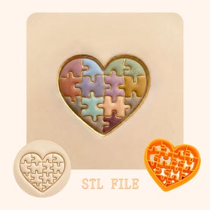 Puede incluir: Un diseño de rompecabezas en forma de corazón con un borde dorado, lleno de coloridas piezas de rompecabezas. Debajo, se muestra un sello de rompecabezas a juego y un cortador en forma de rompecabezas naranja. El texto "STL FILE" está impreso debajo.
