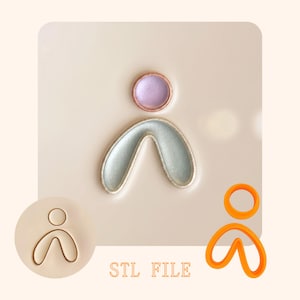 Könnte beinhalten: Ein Ausstechformen-Set bestehend aus einer kreisförmigen und einer bogenförmigen U-Form. Das Set enthält einen 3D-gedruckten orangefarbenen Kunststoffausstecher und einen beigen Stempel, mit einem Beispiel in Lavendel und Hellgrün.