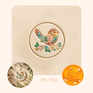 Puede incluir: Un diseño detallado y colorido de un pájaro sobre una superficie redonda y blanquecina. El pájaro, con tonos marrones, turquesas y naranjas, se posa sobre una rama con hojas. La imagen incluye un producto terminado más pequeño y una plantilla de impresión 3D. Texto: STL FILE.