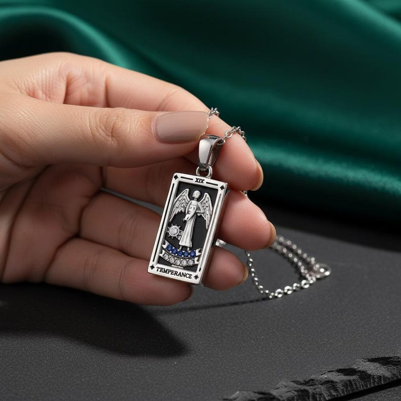 May include: A silver pendant necklace featuring a rectangular tarot card design. The card depicts an angel with wings, the word "TEMPERANCE", and the Roman numeral "XIX". The pendant is on a silver chain.