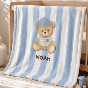 Può includere: Una coperta morbida e felpata con strisce verticali azzurre e bianche. Al centro, un orsacchiotto marrone indossa un berretto da baseball blu e una maglietta a righe blu e bianche. Il nome NOAH è ricamato in marrone sotto l'orsacchiotto.